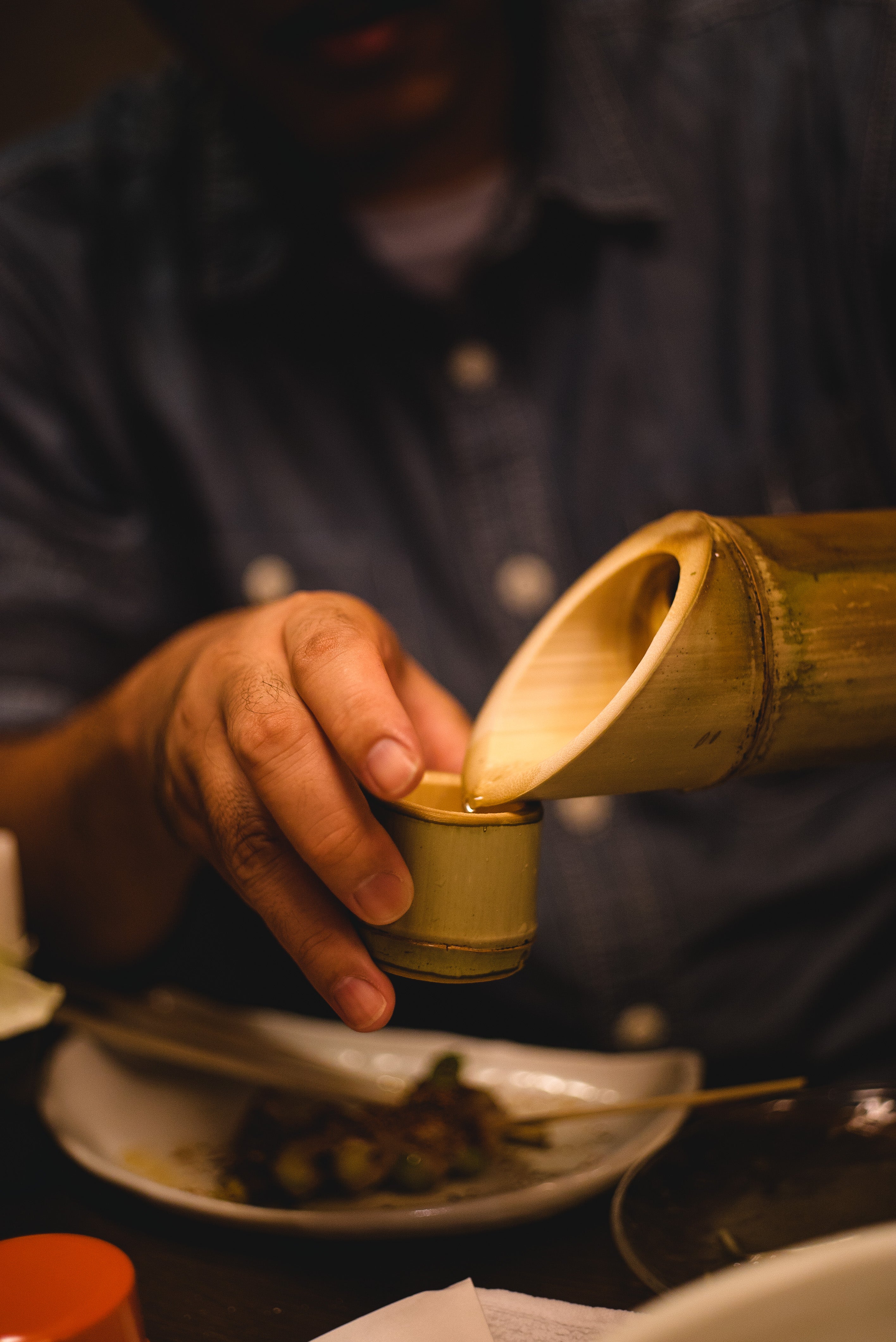 A hand is holding a bamboo cup and pouring water